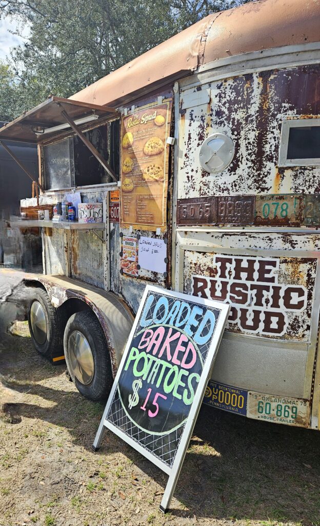 Rustic food truck labeled “The Rustic Spud” with a sign advertising loaded baked potatoes for $15