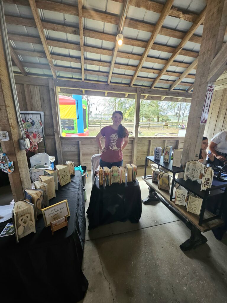 Vendor booth displaying handmade folded book art inside a barn at a local fair