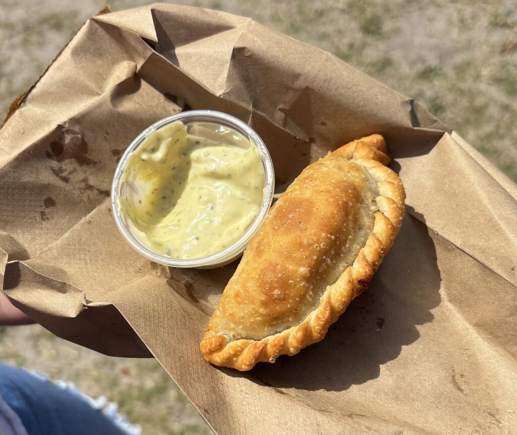 Golden fried empanada served on brown paper with a side of creamy dipping sauce