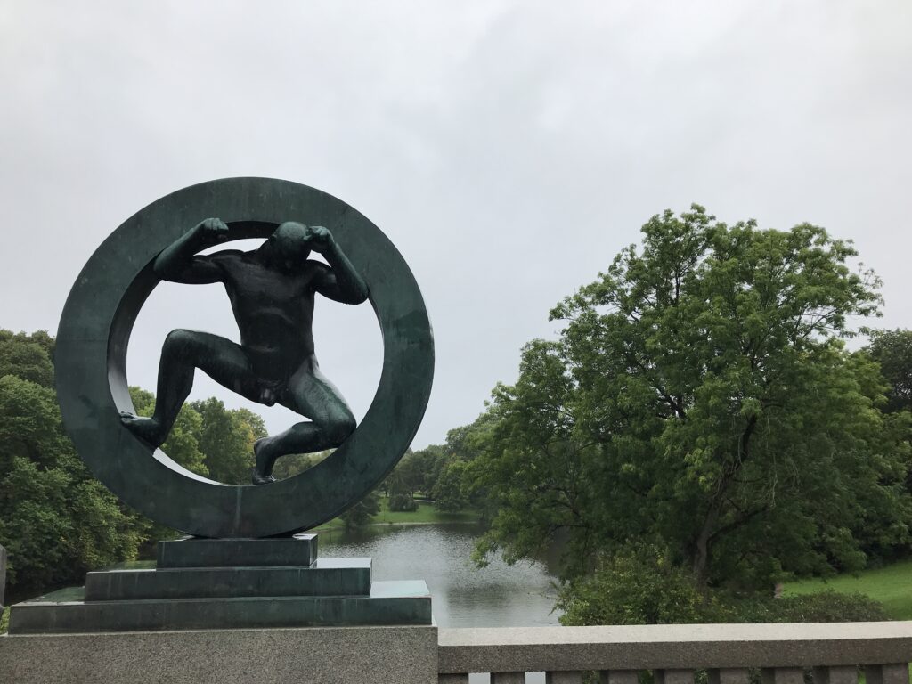 Sculpture of a man inside a circular ring overlooking water in Vigeland Park, Oslo