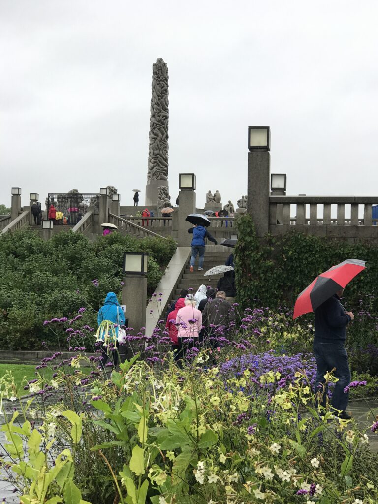 Visitors walking up steps toward the Monolith sculpture in Vigeland Park with umbrellas