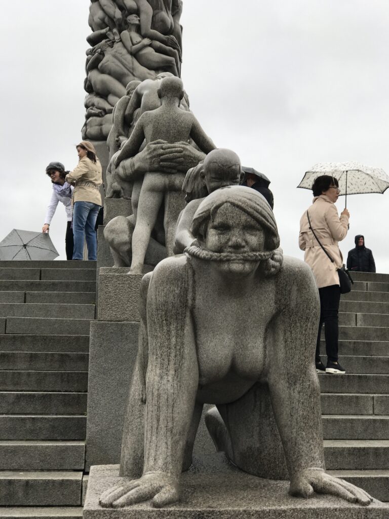 Stone sculpture of a crouching figure with people on steps behind in Vigeland Park