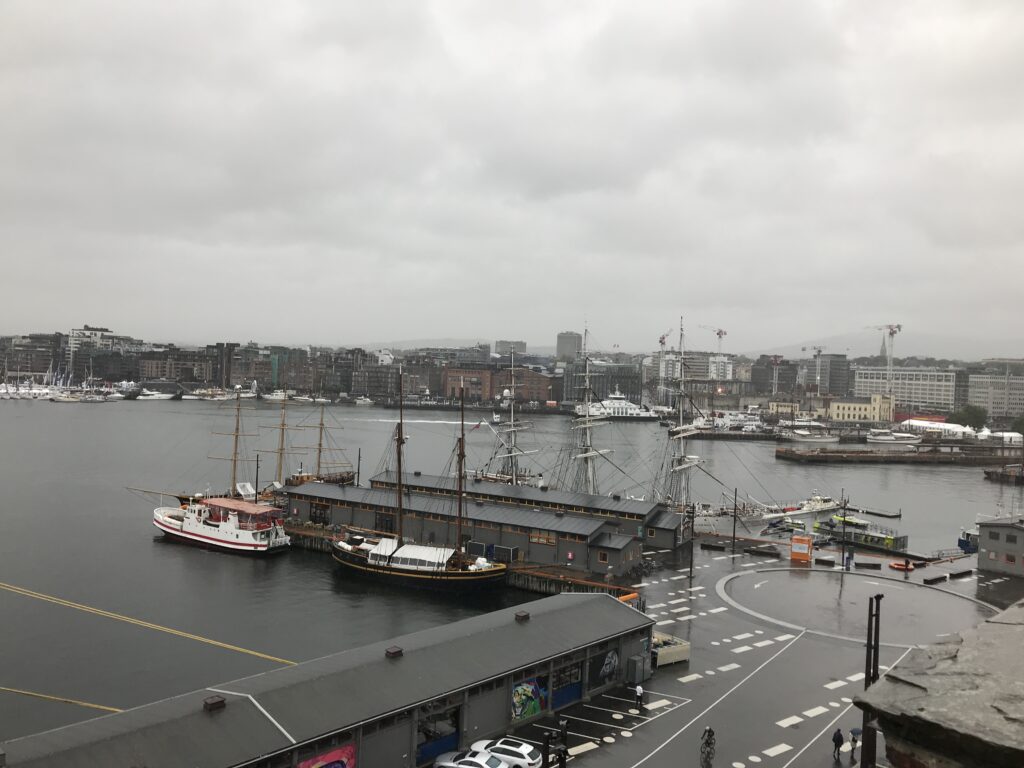 Oslo harbor view with historic ships and waterfront buildings on a rainy day