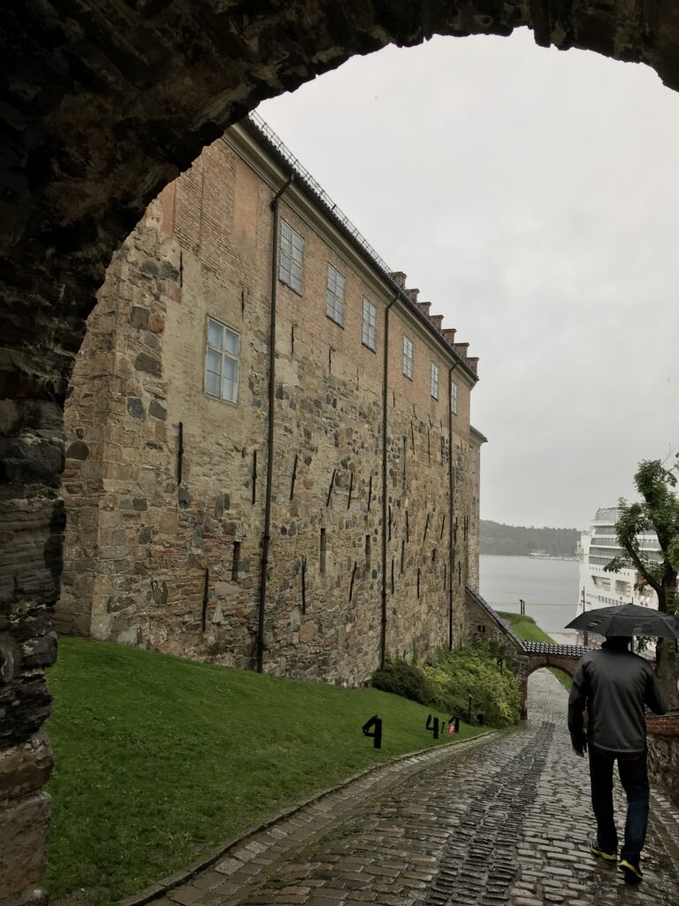Outer fortress wall along waterfront with visitors walking in the rain at Akershus Fortress