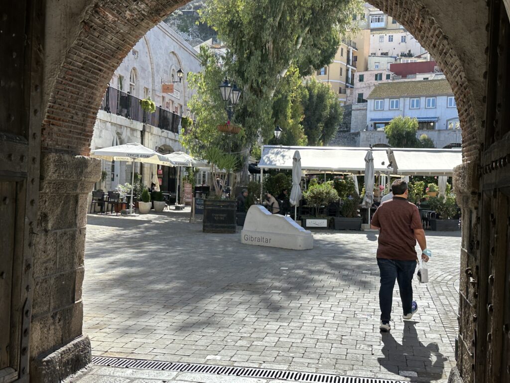 Outdoor cafés and seating in a sunny Gibraltar square with trees and surrounding historic buildings.