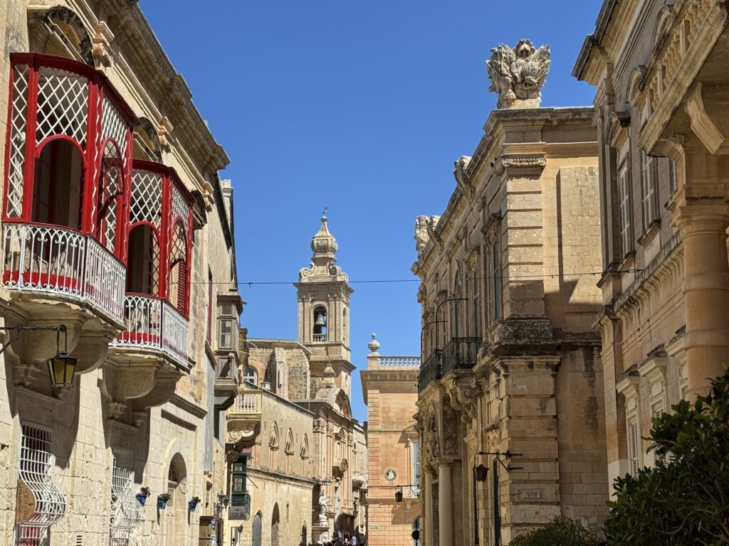 Charming street in Mdina with traditional Maltese balconies and historic buildings leading toward a church tower.