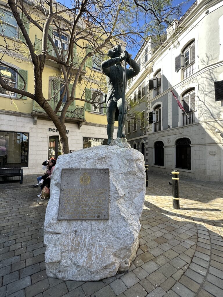 Statue on a stone pedestal in a small square in Gibraltar surrounded by historic buildings.