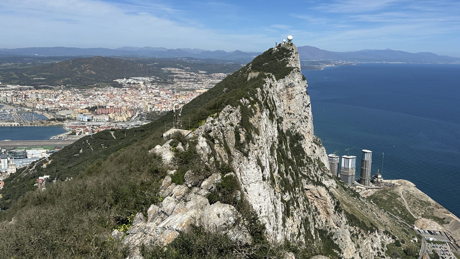 View along the ridge of the Rock of Gibraltar with the city, harbor, and coastline on one side and the Mediterranean Sea stretching out on the other.