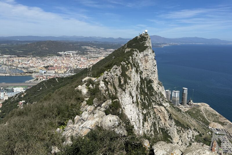 View along the ridge of the Rock of Gibraltar with the city, harbor, and coastline on one side and the Mediterranean Sea stretching out on the other.