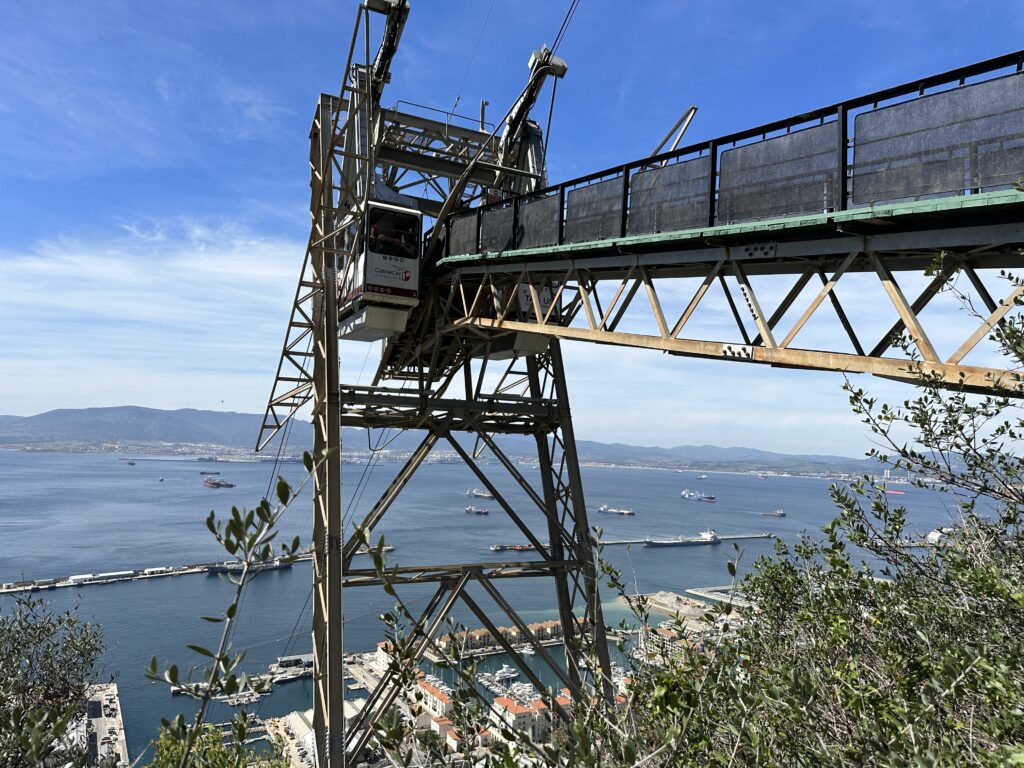 Gibraltar cable car cabin approaching the upper station on the Rock of Gibraltar, with views of the harbor, ships, and coastline stretching across the Mediterranean below.