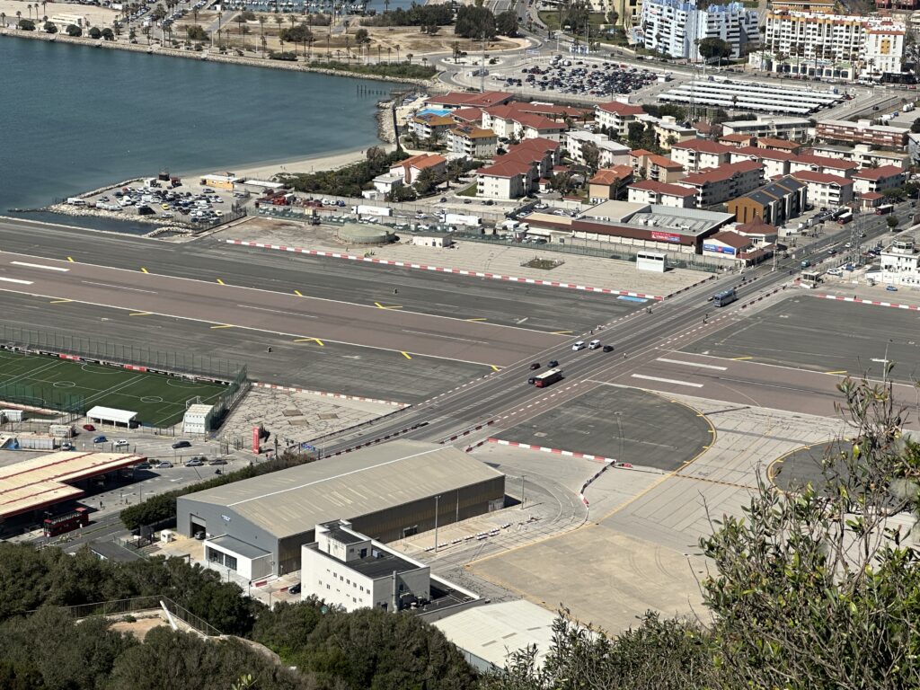 Gibraltar airport runway and road crossing with vehicles, viewed from above on the Rock of Gibraltar.