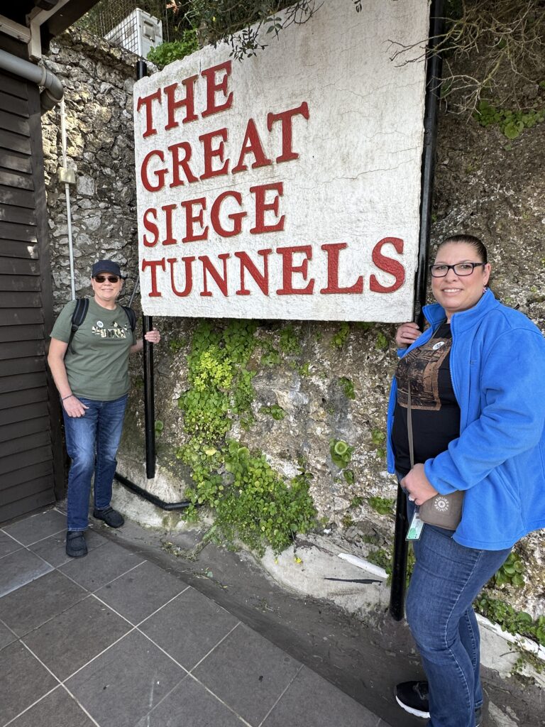 Visitors Pam (left) and Lori (right) standing beside The Great Siege Tunnels sign at the entrance on the Rock of Gibraltar.