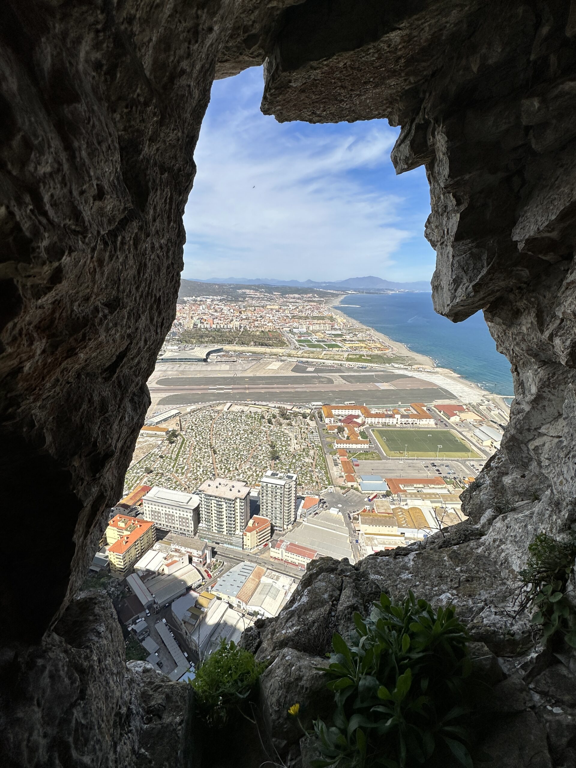 View through a natural rock opening in the Great Siege Tunnels overlooking Gibraltar’s city and shoreline.