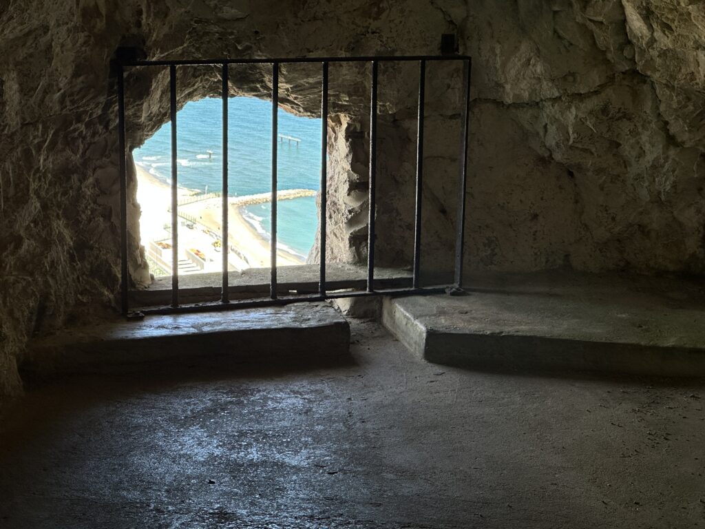 Interior cave room with barred window opening overlooking the sea from the Great Siege Tunnels.