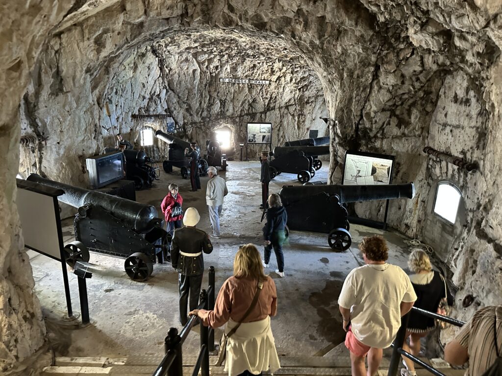 Historic artillery display inside a cave chamber of the Great Siege Tunnels with visitors exploring.