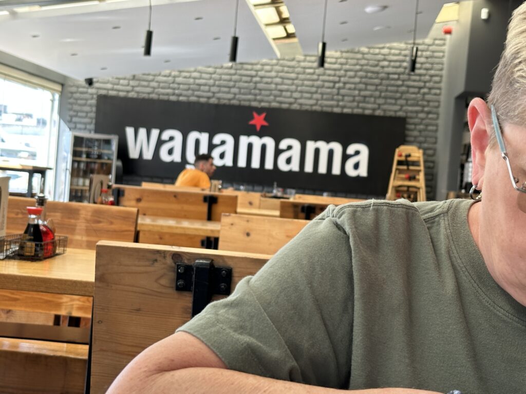 Interior of a Wagamama restaurant with wooden seating and the logo displayed on the wall.