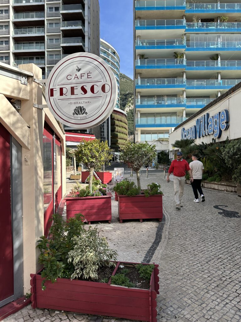 Café Fresco sign along a pedestrian street with modern buildings and outdoor seating in Gibraltar.