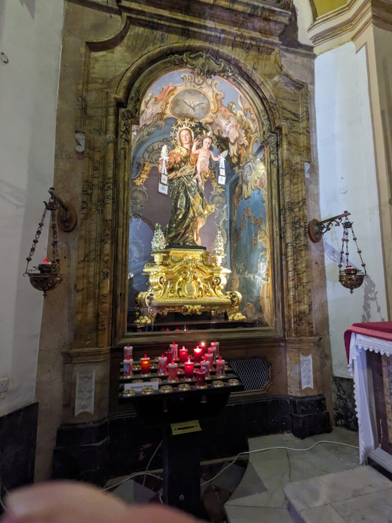 Religious shrine with a statue of the Virgin Mary holding a child, set in an ornate alcove above lit red candles.