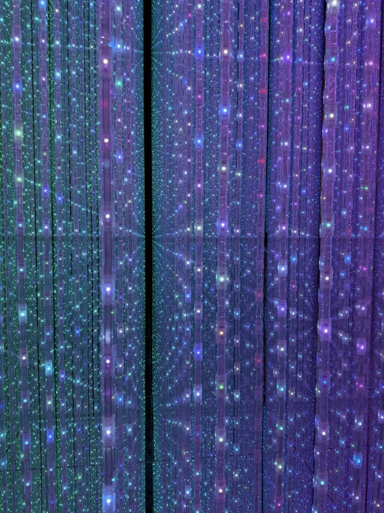 Rows of hanging LED lights glow in green, blue, and purple, creating a vibrant, immersive display with a sense of depth and sparkling reflections.