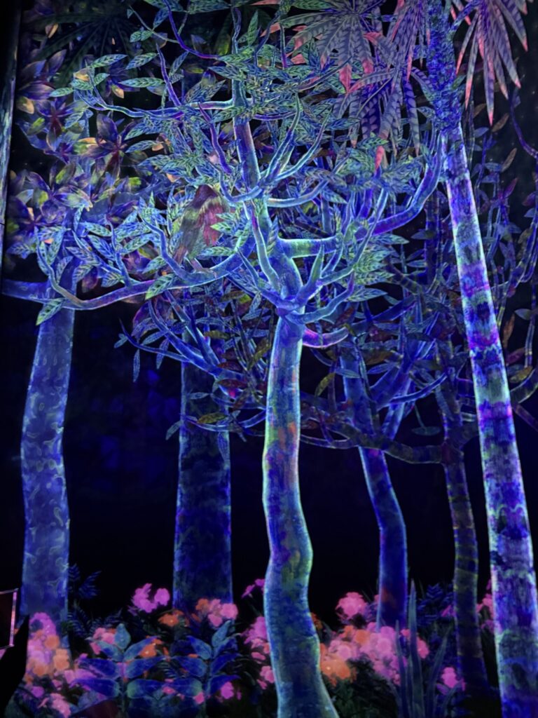 Glowing trees and plants in vibrant neon colors, including blue, purple, and pink, are set against a dark background, creating a surreal, mystical forest scene.
