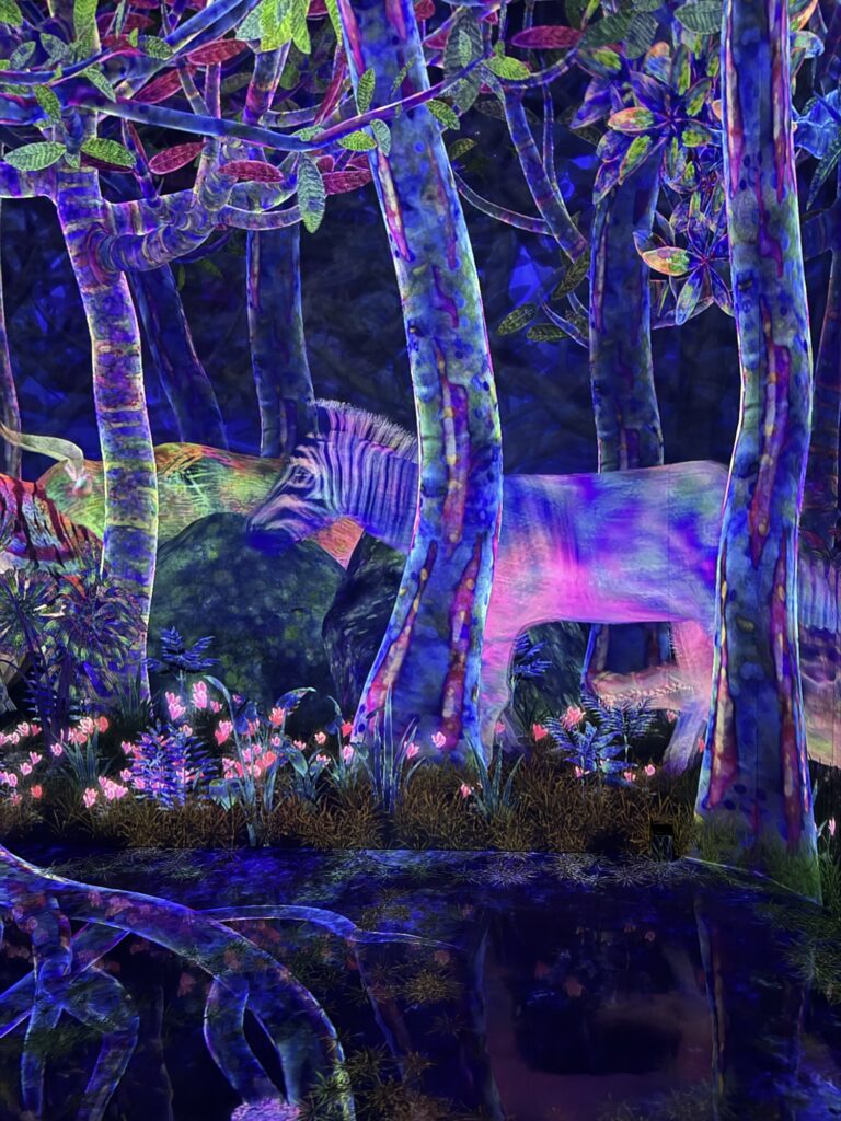 A zebra with glowing, neon purple and blue stripes stands among vibrantly lit trees and flowers in a surreal, colorful forest scene reflected in a pool of water at the bottom.