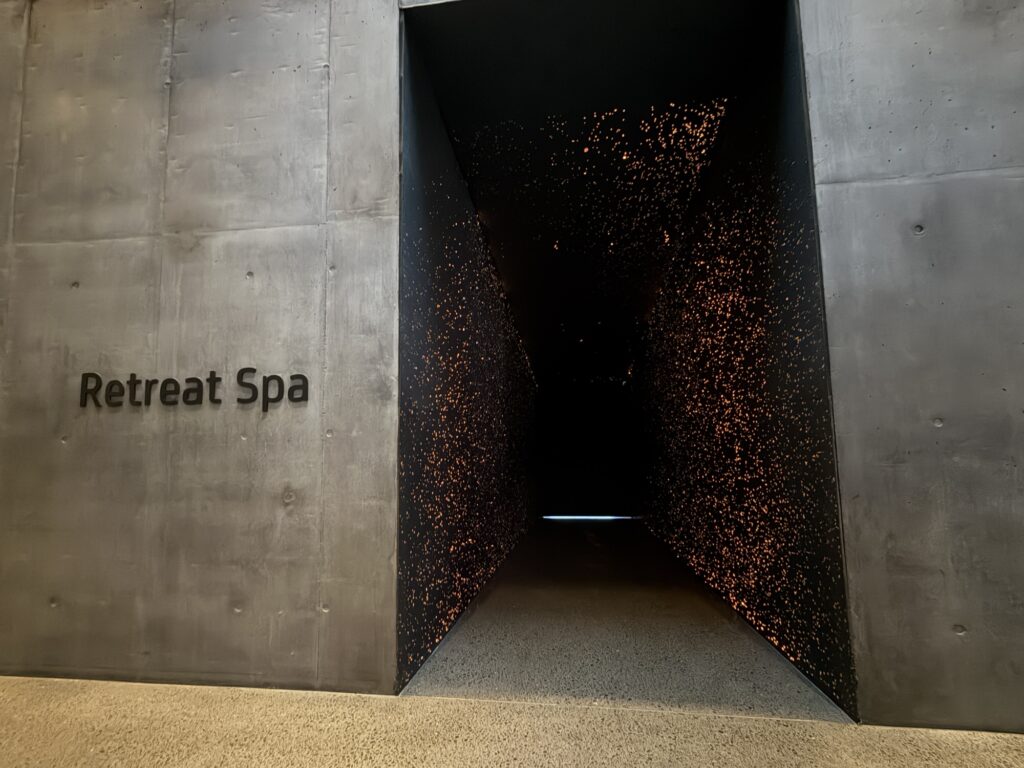 A modern, dark-gray entryway labeled Retreat Spa leads to a dim corridor with scattered warm lights on its walls, creating a tranquil and inviting atmosphere.