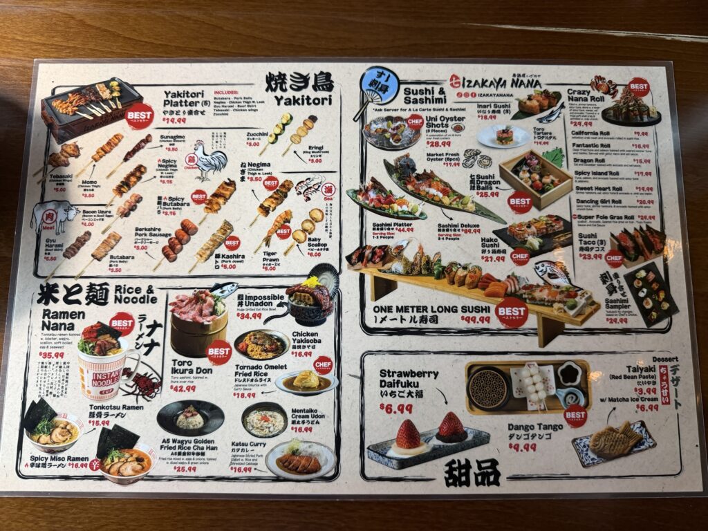 Menu on a wooden table featuring yakitori skewers, sushi and sashimi platters, ramen, rice bowls, desserts, and drinks, with photos of each dish, descriptions, and prices in both English and Japanese.