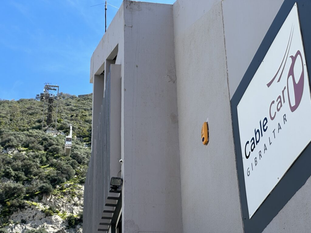 Cable car ascending the Rock of Gibraltar hillside, with the Gibraltar cable car station building and sign visible in the foreground.