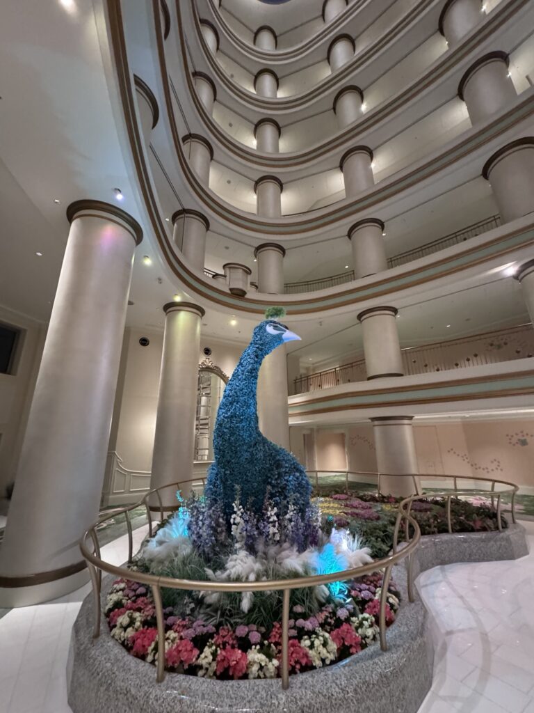 Blue peacock sculpture inside Tokyo DisneySea’s Fantasy Springs hotel lobby surrounded by flowers