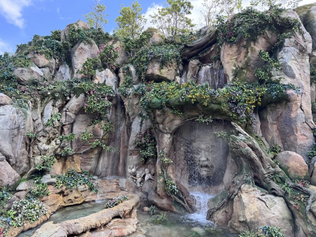 Rock wall waterfall at Tokyo DisneySea featuring a carved face surrounded by greenery and flowing water