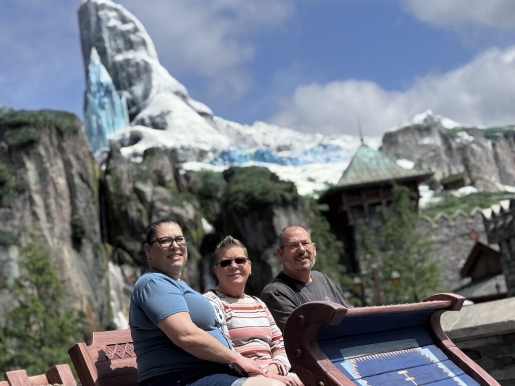 Guests Lori (left), Pam (middle), and Jeff (right) posing in a sleigh at Tokyo DisneySea with snowy mountain backdrop in the distance. Frozen area.