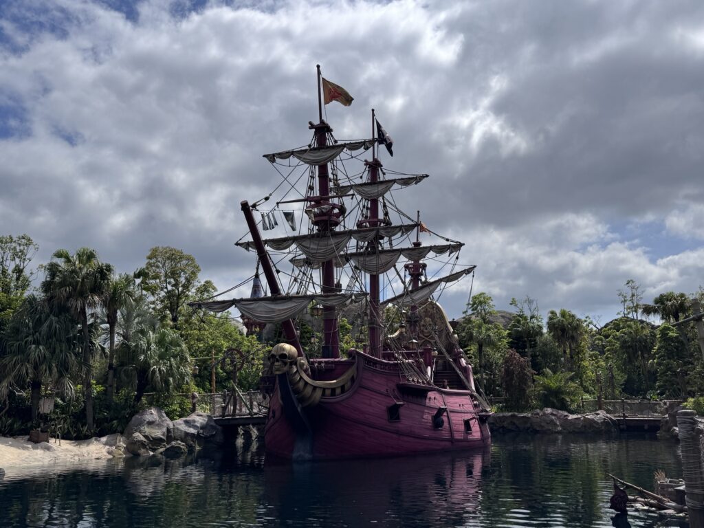 Pirate ship anchored in Tokyo DisneySea surrounded by water and lush greenery under cloudy skies