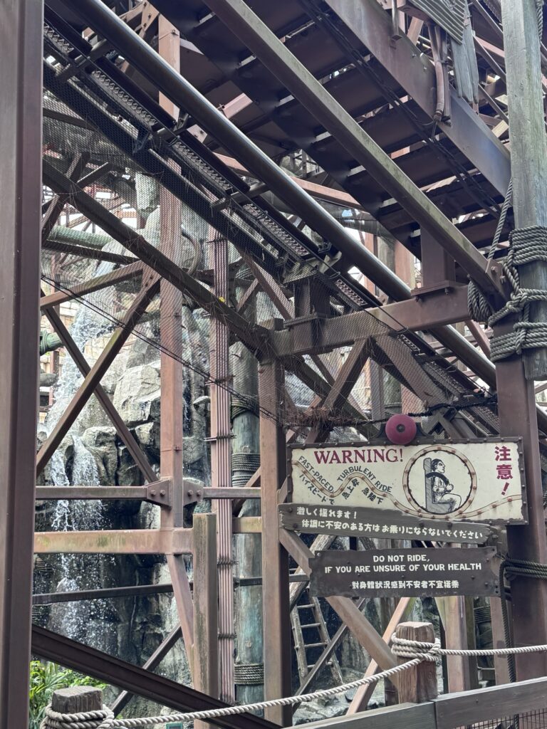 Close-up of warning sign inside Indiana Jones Adventure queue at Tokyo DisneySea with detailed steel structure overhead
