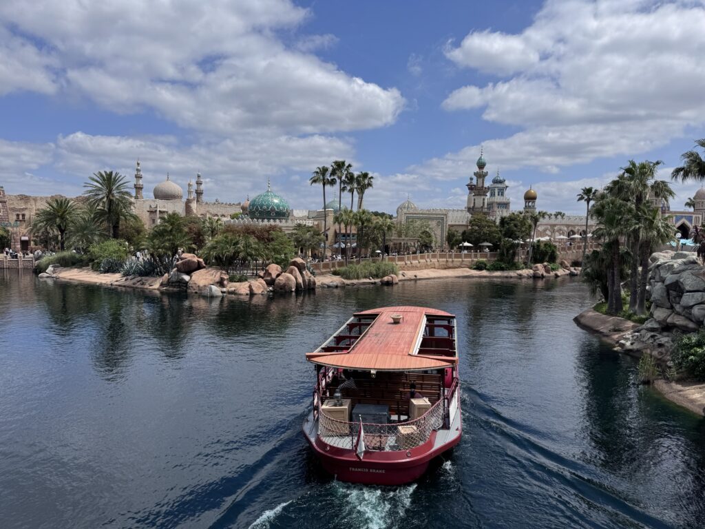Boat crossing Tokyo DisneySea lagoon with Arabian Coast skyline and palm trees in the background