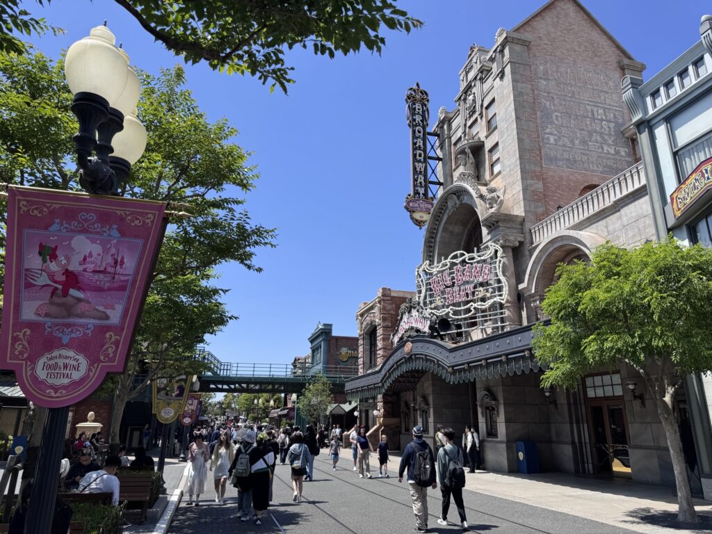 Entrance street at Tokyo DisneySea’s American Waterfront with vintage buildings, banners, and guests walking toward the park