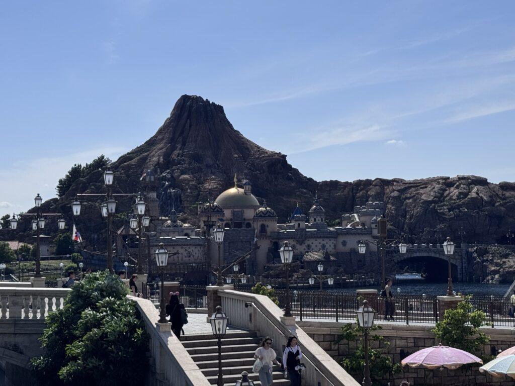 Wide view of Tokyo DisneySea’s Mediterranean Harbor with Mount Prometheus volcano, waterfront buildings, and guests walking along the promenade
