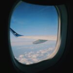 View from an airplane window showing the wing and winglet against a bright blue sky with scattered clouds below.