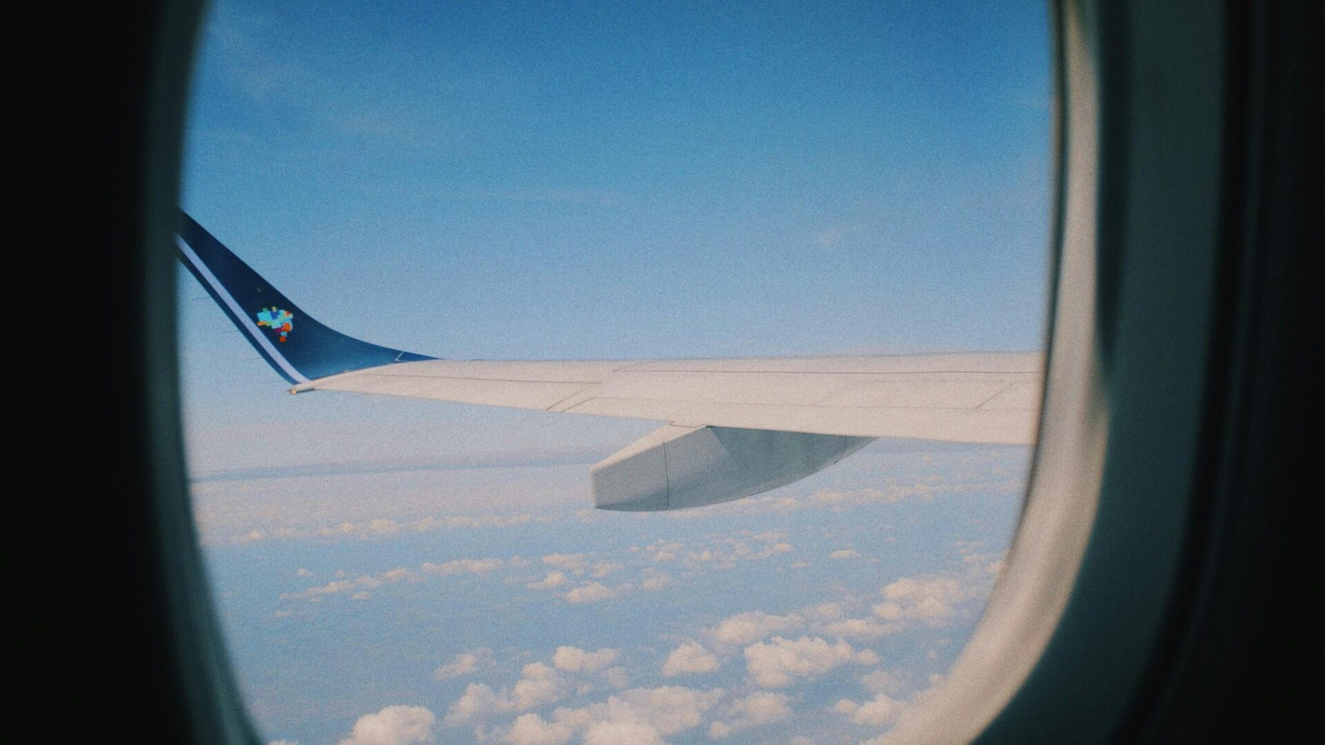 View from an airplane window showing the wing and winglet against a bright blue sky with scattered clouds below.