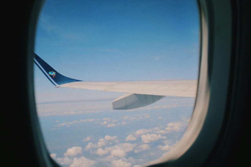 View from an airplane window showing the wing and winglet against a bright blue sky with scattered clouds below.