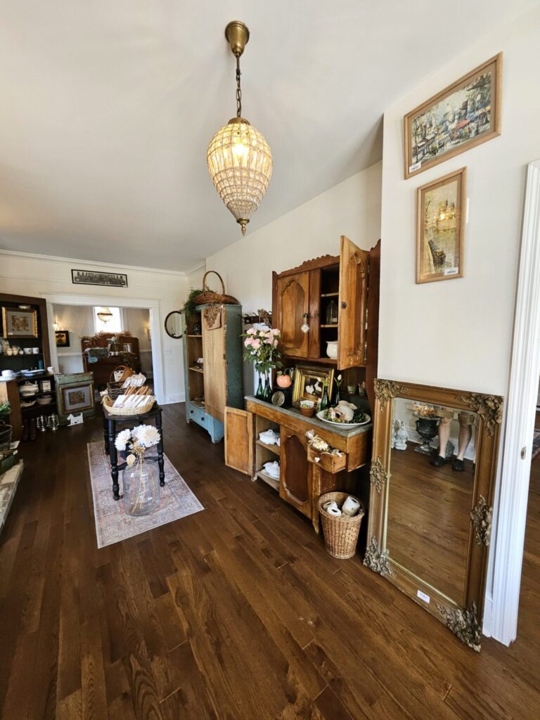 Elegant hallway with dark wood flooring, antique furniture, crystal chandelier pendant light, and framed artwork on cream walls