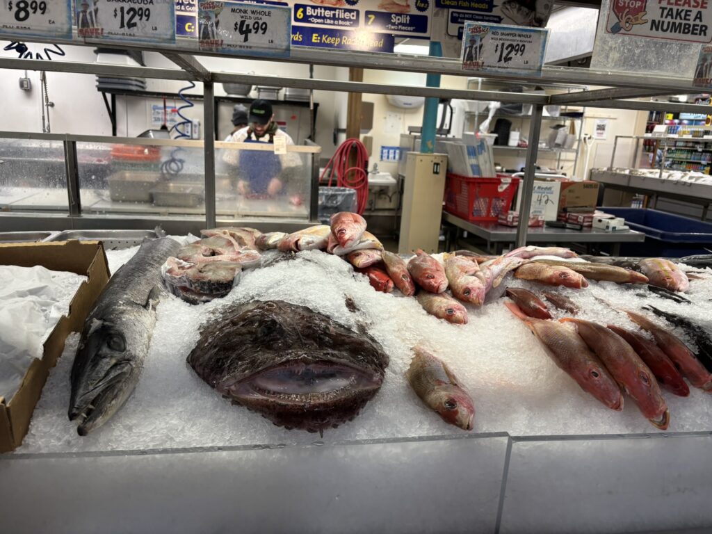 Fresh seafood display on ice at Jungle Jim’s, featuring whole fish and fillets including red snapper, with a fishmonger working behind the counter in the background.