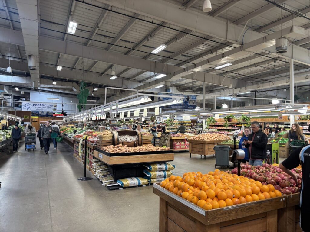Customers shopping the produce department at Jungle Jim's with bins of different fruits including oranges and sweet potatoes.
