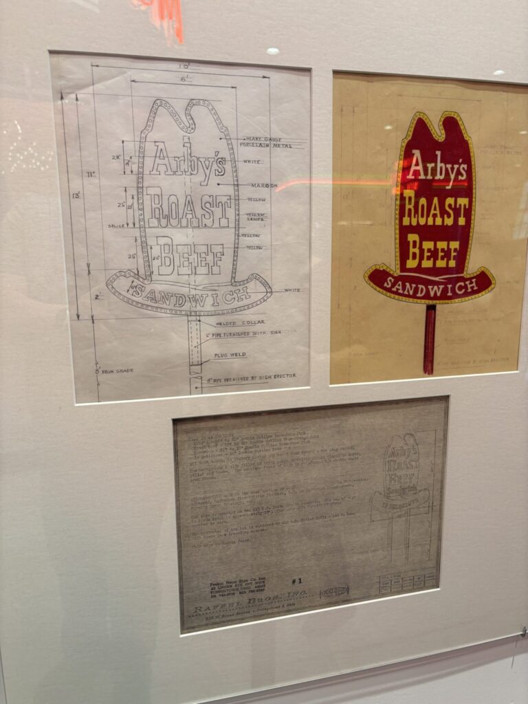 Framed museum display featuring an Arby’s Roast Beef sign, with the original design drawing on the left and the finished colored version on the right.