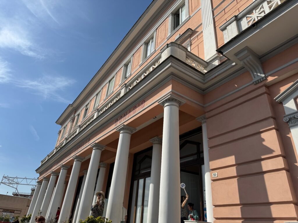 Classical building with terracotta facade, white columns, and ornate cornice under clear blue sky