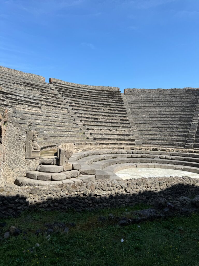 Ancient Roman amphitheater ruins with stone seating tiers and sculptured lion statue under clear blue sky