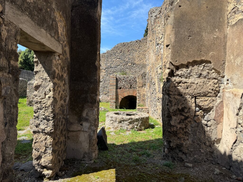 Ancient Roman ruins with stone columns and archways stand amid grassy grounds under blue sky