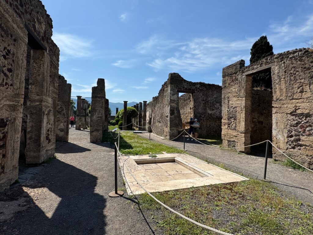 Ancient Roman ruins with stone columns and arched doorways preserved in Pompeii under clear blue sky