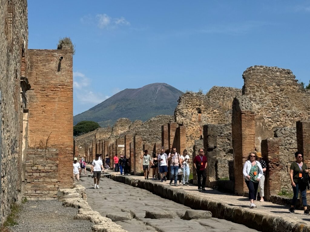 Tourists walk through ancient Roman ruins in Pompeii with Mount Vesuvius visible in the background
