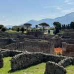 Ancient Roman stone ruins with brick walls in foreground, green landscape and mountains visible beyond in Pompeii