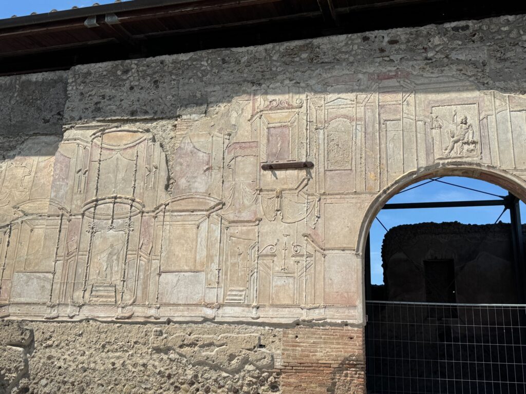Ancient stone relief carving with decorative geometric patterns adorns a weathered wall beside a modern arched doorway
